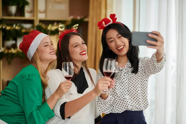 Team of joyful colleagues drinking wine at taking funny selfies at Christmas party