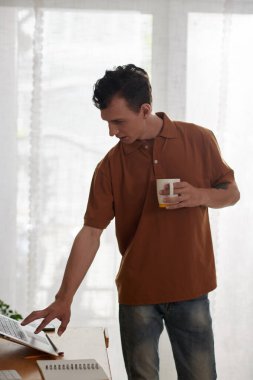 Laptop 'a rapor yüklerken sabah kahvesi içen genç adam.