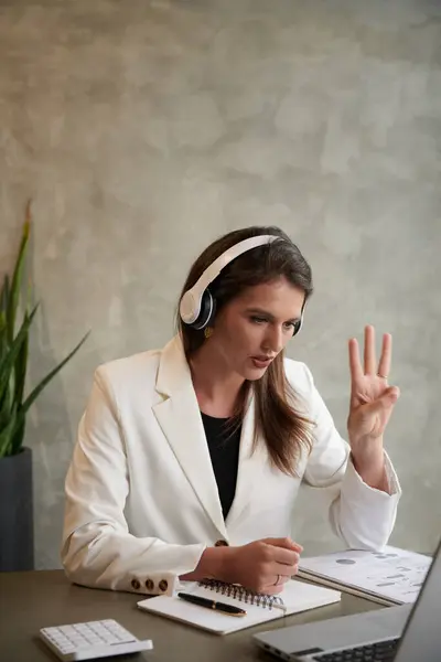 Young elegant businesswoman showing three fingers when talking to colleague in online meeting