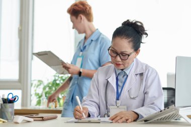 Hastaları muayene ettikten sonra dokümanları dolduran ciddi bir pratisyen.