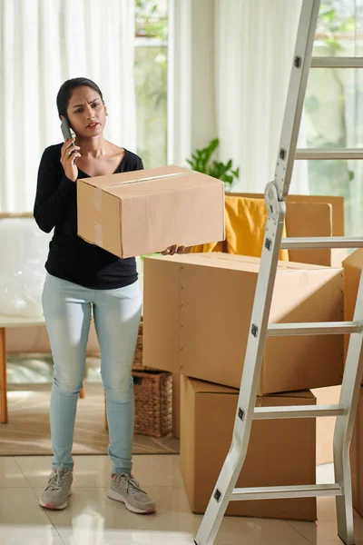 Frowning woman packing belongings and calling to moving company