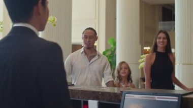 Üç kişilik çok kültürlü bir ailenin, otel resepsiyonistine seyahat sırasında belgelerini verirken orta ölçekli bir fotoğrafı.