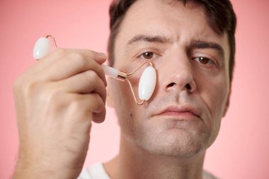 Olgun bir adamın portresi Quartz silindirle yanaklarına masaj yapıyor.