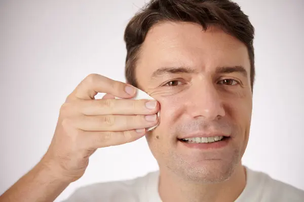 Smiling mature man wiping face with cotton pad with toner to balance skin ph