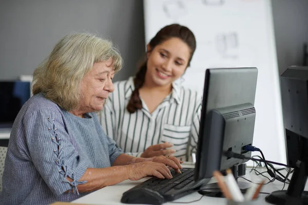 Elderly woman typing on computer under control on teacher