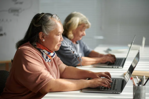 コンピュータクラスのタスクの1つとしてラップトップに電子メールを書く集中的な年齢の女性 — ストック写真
