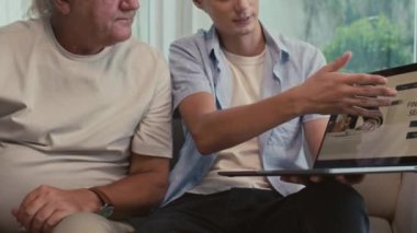 Finansal hizmetler web sitesi açık olan kablosuz bilgisayarı elinde tutarken genç adamın olgun babasıyla konuşurken görüntüsünü kaldır.