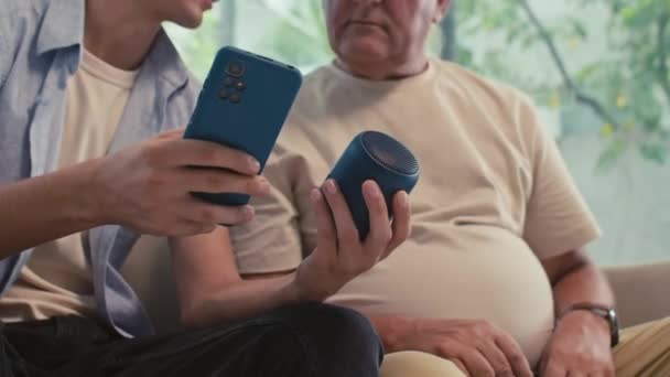 スマートスピーカーと携帯電話の間のワイヤレス接続で年金受給者を支援する男のクロップショット — ストック動画