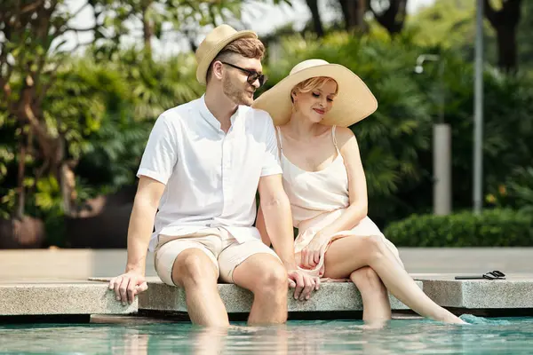 Young couple putting their feet in the water and enjoying summer vacation by the outdoor pool