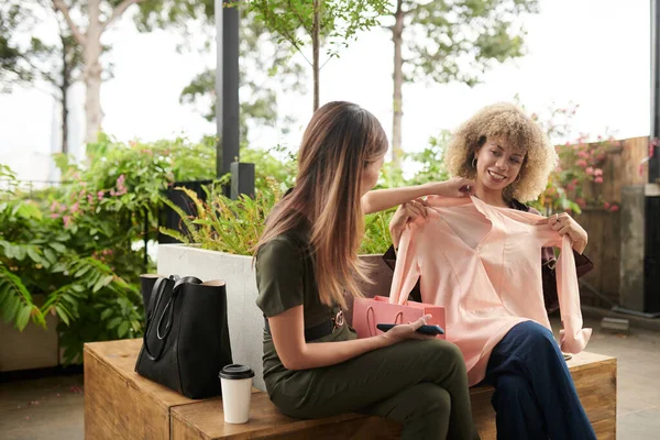 Young woman showing her new blouse to friend during their meeting in outdoor cafe