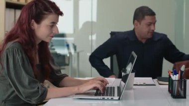 Konferans odasında erkek direktörle görüşürken bilgisayarını kullanan neşeli kadın çalışanın yan görüntüsü