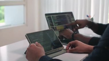 Programcı ve yönetmenin dijital tablet ve dizüstü bilgisayardaki program koduna bakarken masada yan yana otururken görüntüsü kesilmiş.