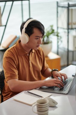 Genç Vietnamlı testçi ofis masasında çalışırken müzik dinliyor.
