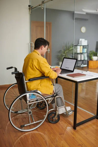 Young man with disability coding on laptop in modern office