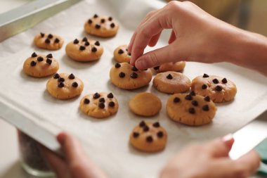 Kurabiyeleri çikolata parçacıklarıyla süsleyen kadının yakın plan resmi.