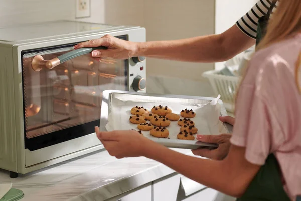Mother and daughter putting tray with cookies in oven