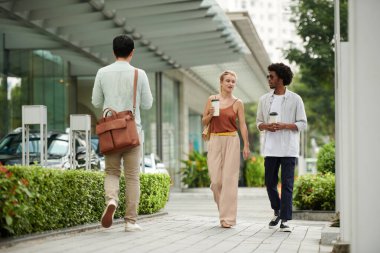İş arkadaşları sabah ofise yürürken kahve içip haberleri tartışıyorlar.