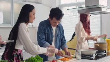 Bir adamın dijital tabletten tarifini kontrol ederken ve kız arkadaşına yardım ederken, diğerleri sebze kesip yemek pişirirken.