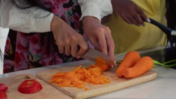 サラダを調理し 家庭のキッチンで話している間 ニンジンやトマトを切断する多民族の女性のトリミングショット — ストック動画