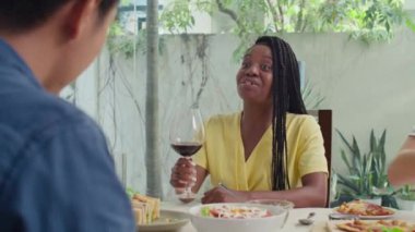 Omzunun üzerinden, çok ırklı çiftler kırmızı şarapla bardaklarını tokuştururken arkadaşlarıyla masaya oturuyorlar, önemli bir olayı kutluyorlar.