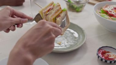 Başkalarıyla yemek yerken kanepeden sandviçi kaldıran tanınmayan bir insanın ellerini kapatın.