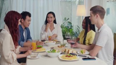 Memleketteki şenlik masasında kutlama yaparken kırmızı şarap ve portakal suyuyla bardakları tokuşturan çok kültürlü arkadaşlar grubu.