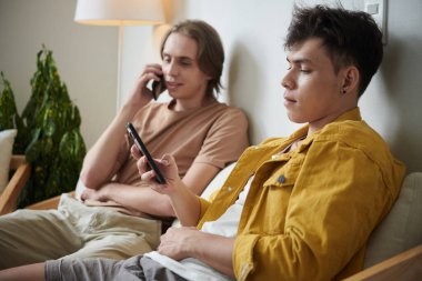 Arkadaşı telefonla konuşurken akıllı telefondan bildirileri kontrol eden genç bir adam.