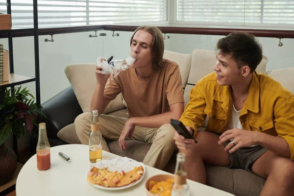 Positive young people smoking vape, drinking beers and watching tv show at home