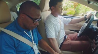 Eğitmenin, genç bir öğrencinin sürüş becerilerini değerlendirirken, arabanın içinde otururken çekilen görüntüsü.
