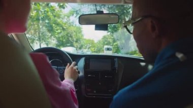 Öğretmenin direksiyon dersi sırasında arabanın içinde otururken dikiz aynasını düzeltmesine yardım ettiği kesikli fotoğraf.