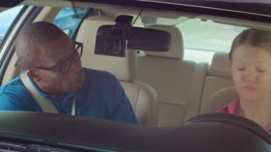 Sürücü eğitmeninin öğrencisiyle konuştuğu ve ders sırasında emniyet kemerini bağlamasını istediği orta boy bir fotoğraf.