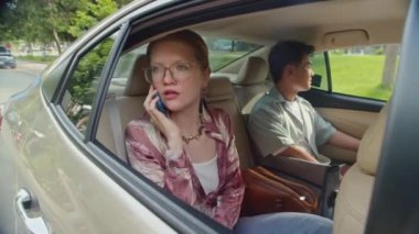 Akıllı telefondan konuşan genç bir kadının yan görüntüsü. Yolcu koltuğunda erkek arkadaşının yanında oturuyor.