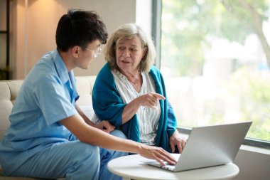 Gülümseyen tıp çalışanı, kıdemli bir kadının tıbbi belgeleri internetten doldurmasına yardım ediyor.