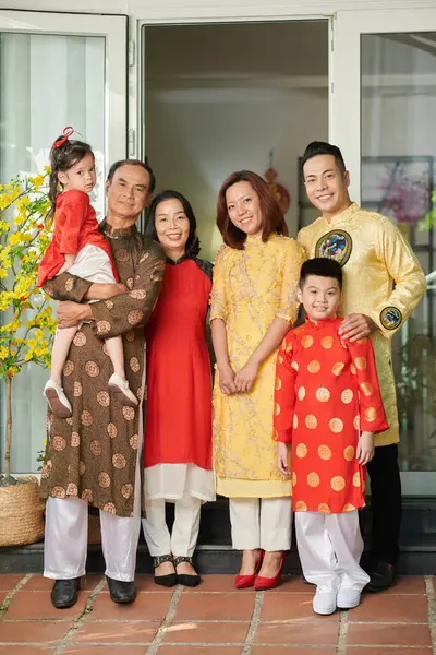 Happy big Vietnamese family in traditional ao dai dresses standing at house entrance
