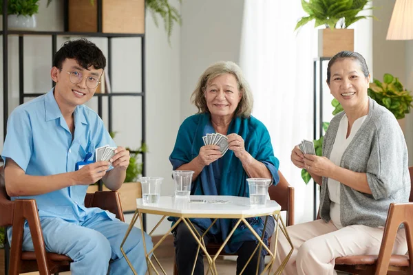 stock image Smiling nurse playing cards with patients of nursing home in lounge area