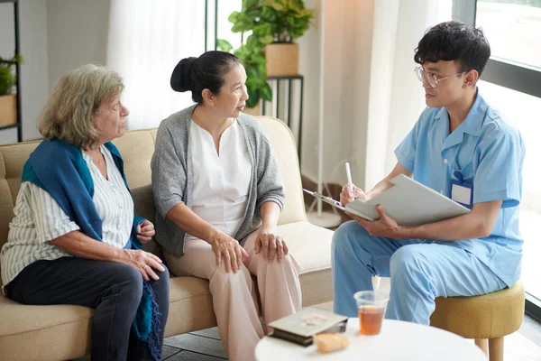 Nursing home doctor talking to senior patients and taking notes in document