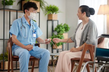 Doktor yaşlı bir kadının tansiyonunu ölçerken elektronik tonometre kullanıyor.