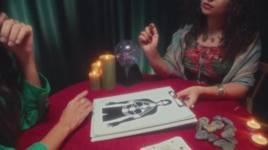 Kâhinin, iyileşme sürecinde elinde mumlarla masada oturan bir kadına vücut grafiği gösterirken orta ölçekli bir fotoğrafı.