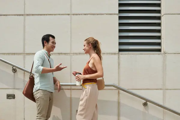 Smiling young Asian man asking out young woman when that are standing on steps outdoors