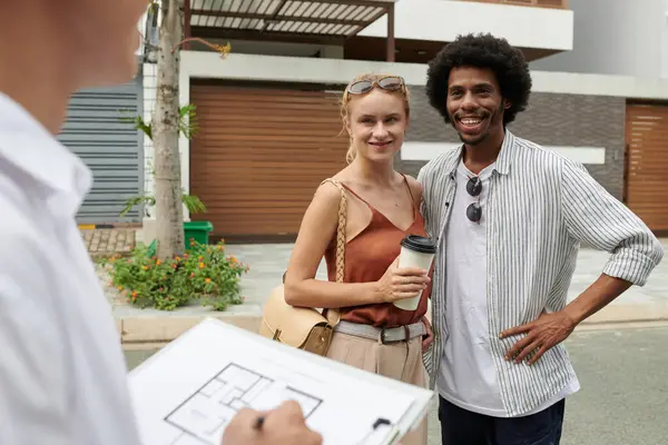 Cheerful couple discussing plan of house they are going to watch with estate agent