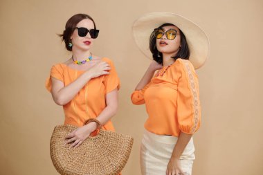 Güneş gözlüklü mankenlerin portresi. Turuncu yaz kıyafetleriyle kameraya poz veriyorlar.
