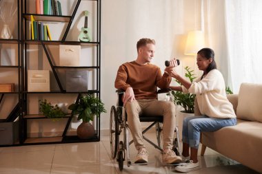 Fizyoterapist, engelli bir adama kaslarını çalıştırmak için dambıllarla nasıl egzersiz yapılacağını gösteriyor.