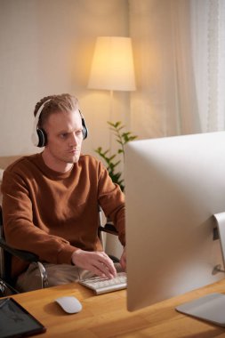 Masada bilgisayar başında çalışırken kulaklık takan ciddi bir genç adam.