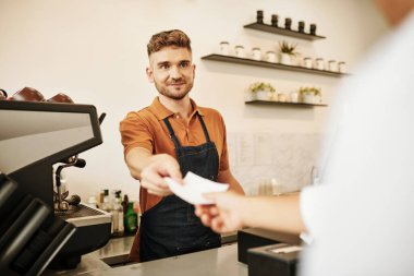Kot önlüklü kahveci müşteriye peçete veriyor.