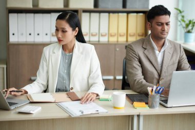 Modern ofiste masa başında çalışan çok ırklı, ciddi bir çift.