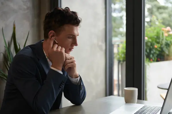 Serious young entrepreneur wearing earbuds when calling business partner