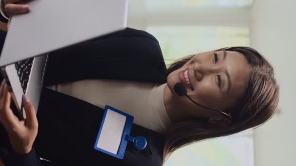 ヘッドセットの陽気な女性アナリストがノートパソコンを使った同僚とのビデオ通話で話す垂直ショット — ストック動画