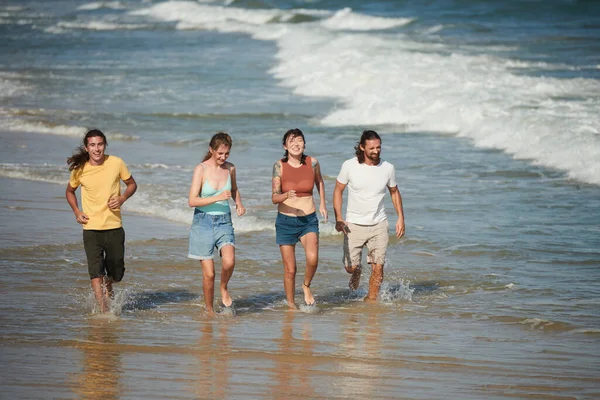 Joyful young people running on beach, splashing water and laughing