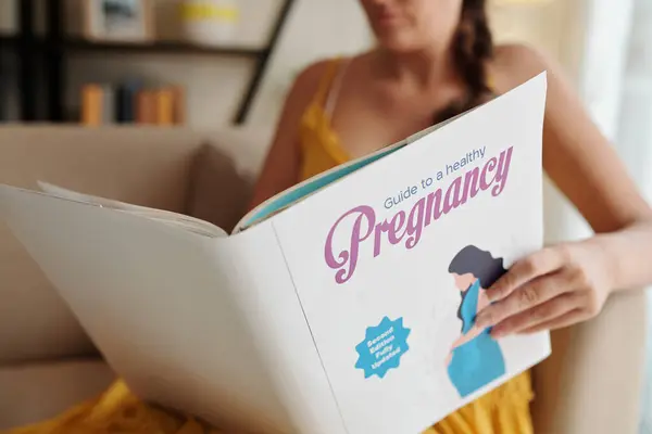 健康な妊娠に関するガイドを読んでいる若い女性のクロップされたイメージ — ストック写真