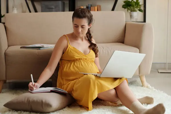 怀孕妇女在家学习 看网络研讨会和在笔记本上写字 — 图库照片